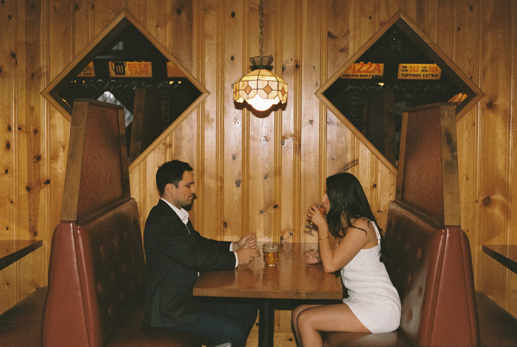 Documentary-style film photo of a couple sharing drinks in a cozy wood-paneled booth at Lloyd’s in Atlanta, captured with natural vintage tones and ambient lighting.