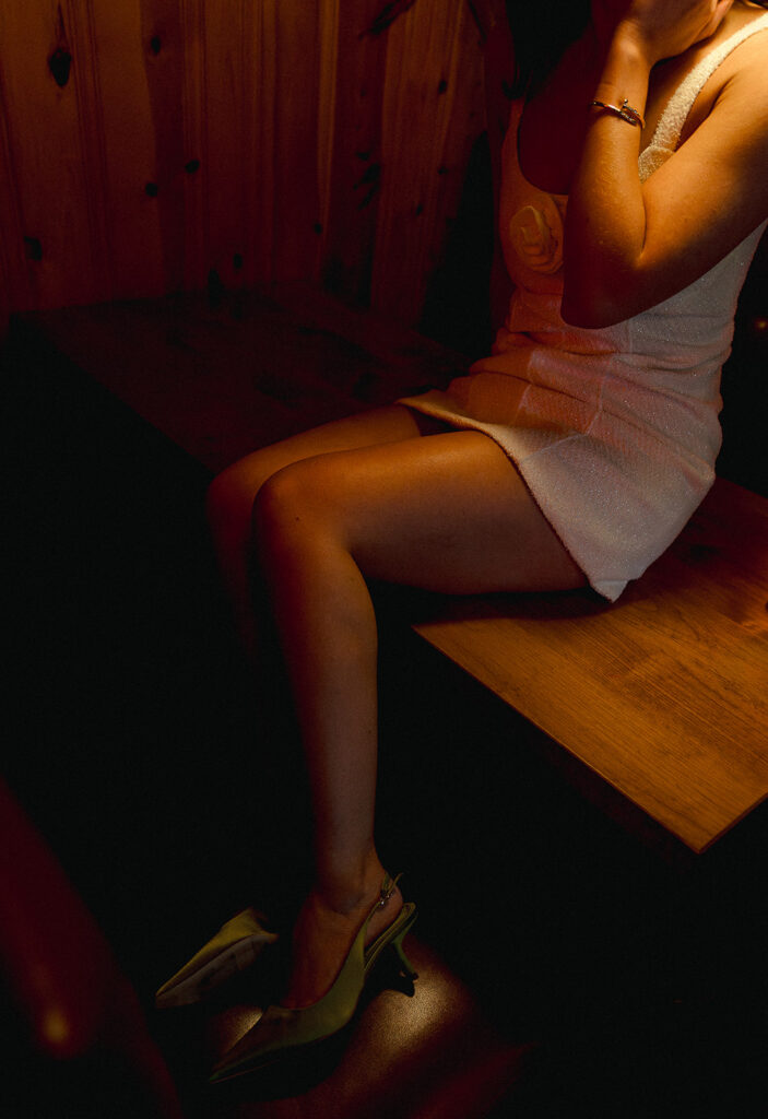 Cinematic engagement detail photo of a woman seated in a retro Atlanta bar booth wearing a sparkly mini dress and green heels—documentary wedding photographer in Atlanta capturing intimate, editorial-style moments.
