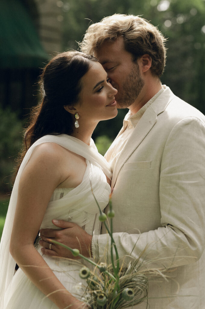 The couple shares an intimate moment in front of an ivy-covered stone wall of the Swan House, gently leaning into each other in the soft afternoon light.