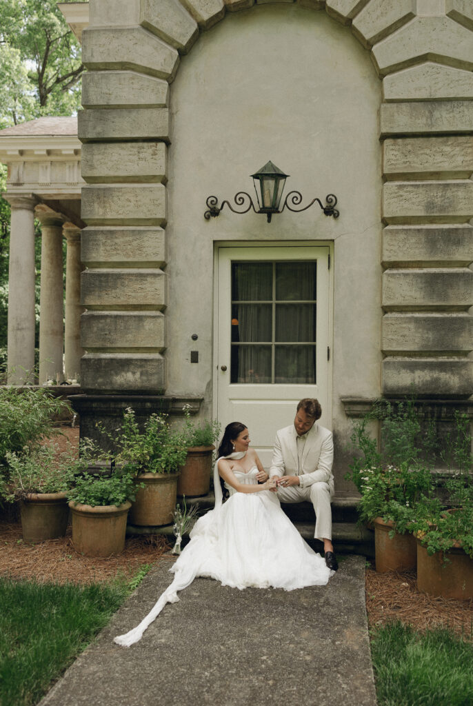 The couple pauses by a stone balustrade in the garden of the Swan House, sharing a quiet conversation surrounded by decorative urns and lush greenery.