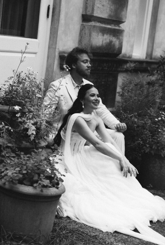 The couple pauses by a stone balustrade in the garden of the Swan House, sharing a quiet conversation surrounded by decorative urns and lush greenery.
