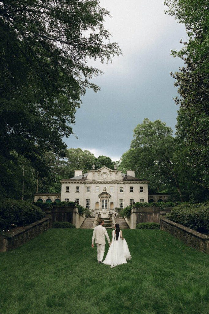 The rear view of the Swan House, showcasing a grand, cascading double staircase that opens onto a manicured lawn. The back of the mansion includes tall, shuttered windows and classical detailing, surrounded by lush greenery and a peaceful garden setting.