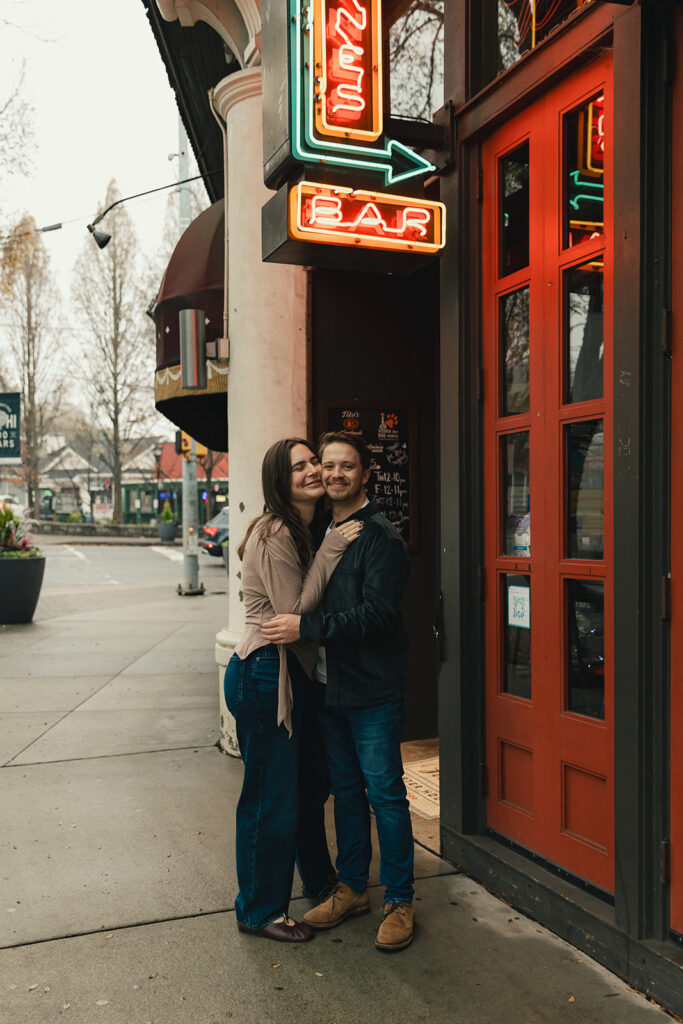 Peyton and Collin hugging in front of a lit-up storefront in Virginia Highlands