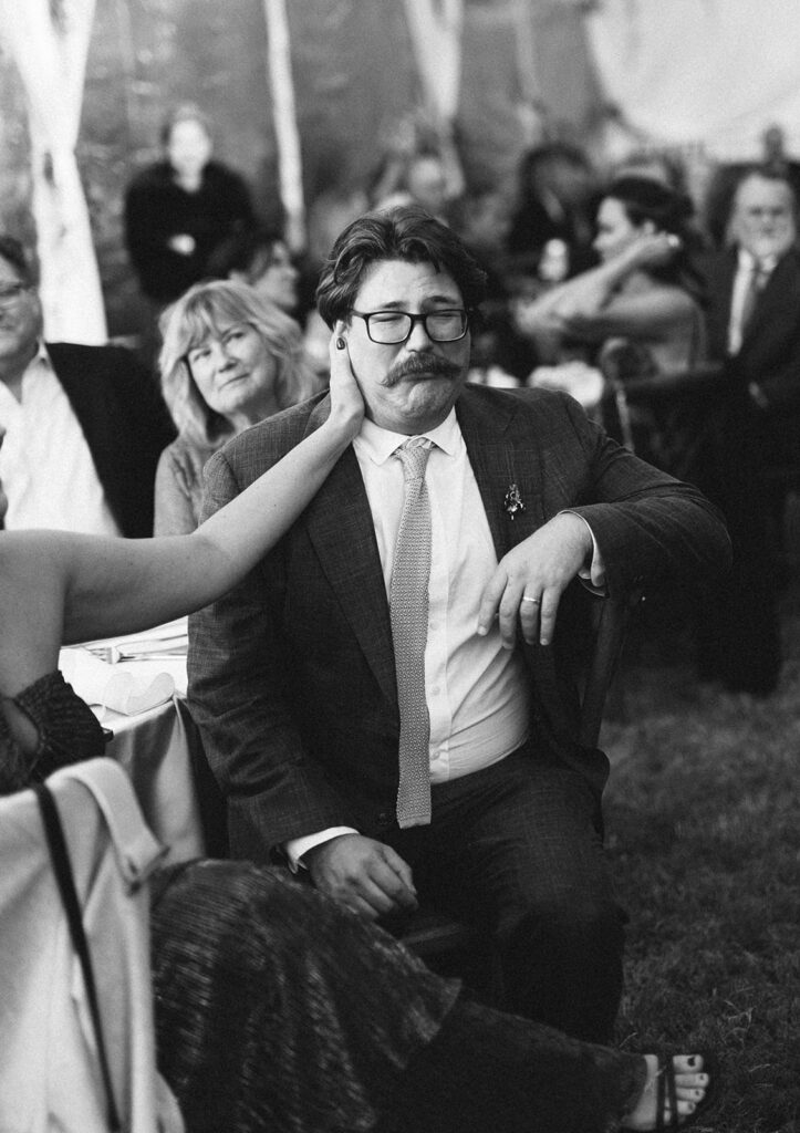 Black and white candid of a guest touching a man’s face lovingly during the wedding reception