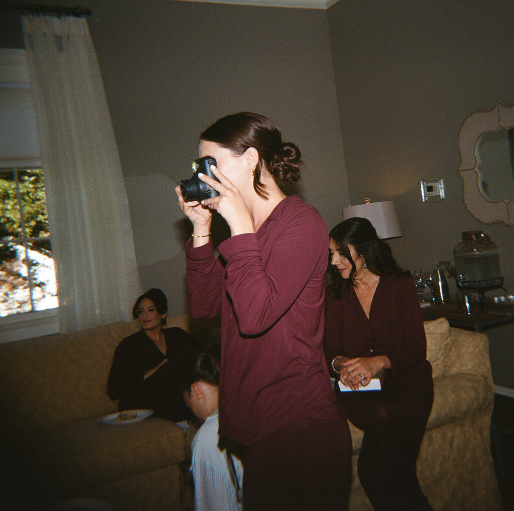Bridesmaid in burgundy pajamas taking a candid photo with an instant camera while getting ready
