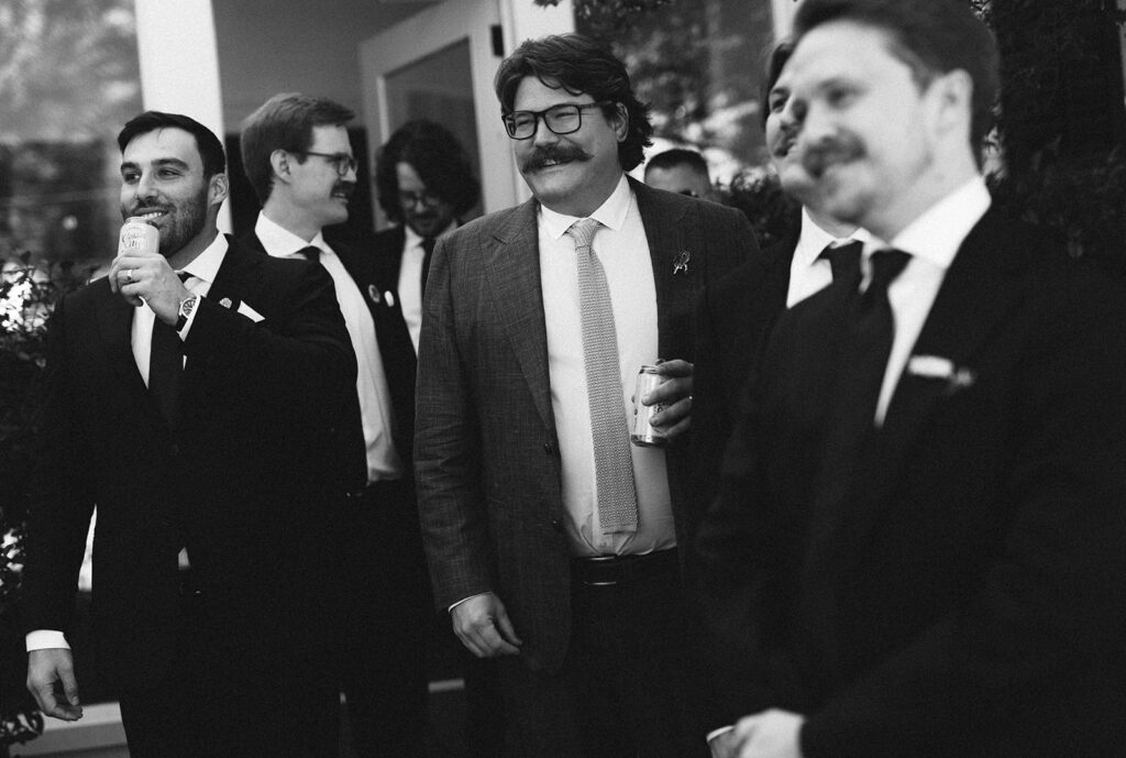 Black and white candid of groomsmen laughing and talking together while holding drinks