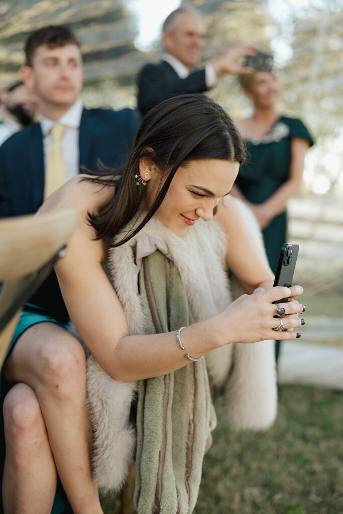 Wedding guest smiling as she takes a photo during the reception, surrounded by family and friends