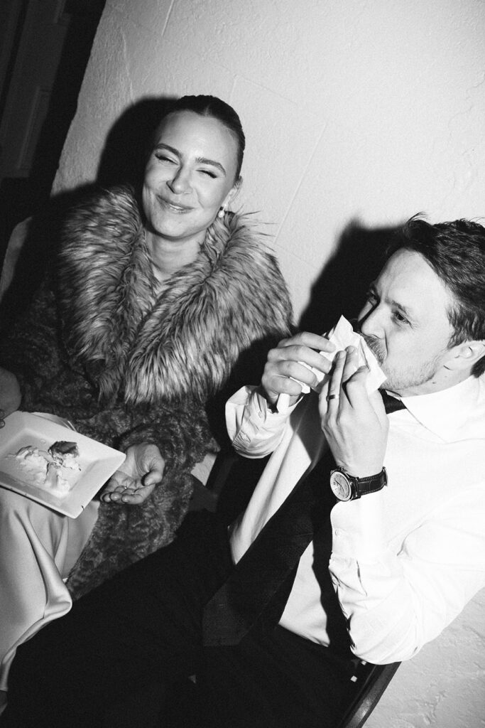 Black and white candid of bride and groom sharing a playful late-night cake moment during the reception