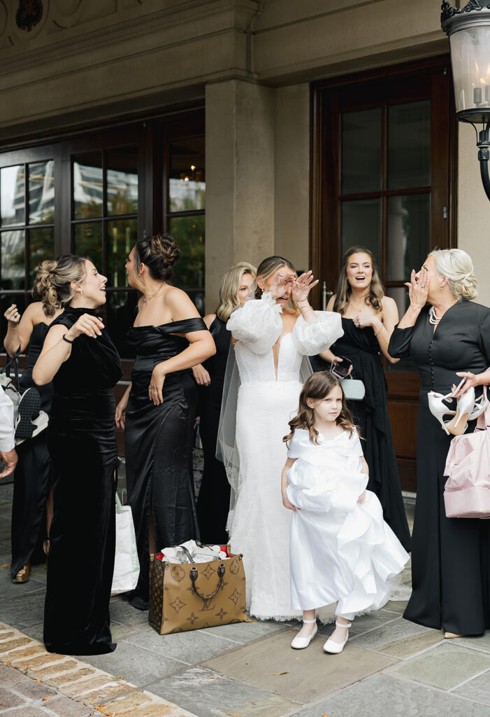 Bride standing with wedding party outside a venue, surrounded by movement, laughter, and anticipation before the ceremony.