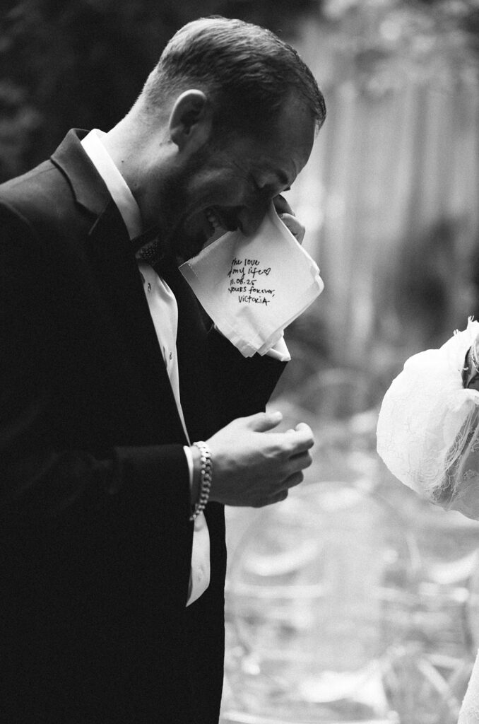 Black and white close-up of a groom holding a handwritten note during an emotional moment at the ceremony.
